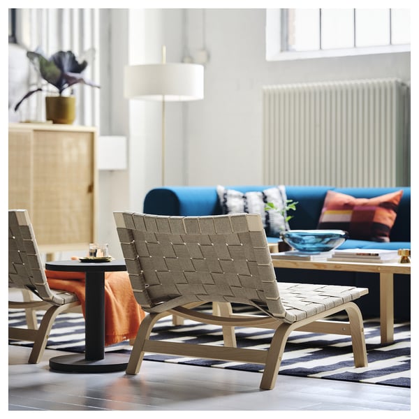 Moderne woonkamer met lichthouten fauteuil, geweven linnen zitting, blauwe bank en gestreept vloerkleed.