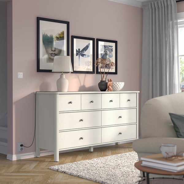 Wit STOREMOLLA dressoir tegen paarse muur met 6 lades, ingelijste foto's, lamp en stoel.