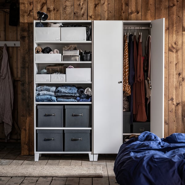 Witte kast met grijze stoffen lades, netjes georganiseerde kleding. Houten muur achtergrond.