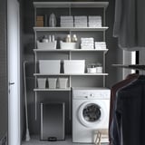 Georganiseerde kast SULTEN RVS pedaalemmer naast een witte wasmachine, omgeven door netjes gerangschikte planken met wasartikelen.
