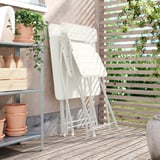 Drie witte klapstoelen netjes gestapeld op een houten balkon. De stoelen hebben een eenvoudig, modern ontwerp, perfect voor kleine ruimtes.