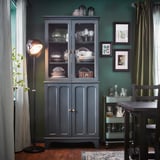 Gezellige eetkamer met groene muren, donkerhouten meubels, een zwarte lamp en ingelijste foto's.