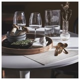 Elegante tafelsetting met SVARTSENAP grijze placemat, houten dienblad, gouden keukengerei en wijnglazen.