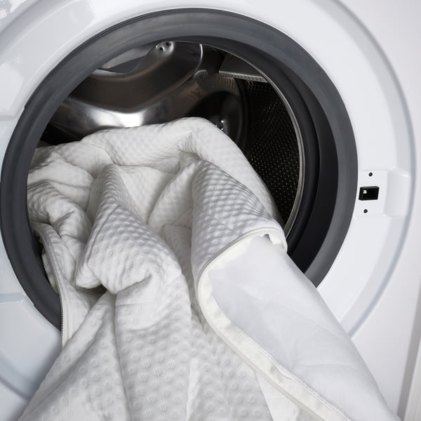 Wit beddengoed in de deur van de wasmachine, klaar om schoon te maken.