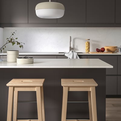 Moderne keuken: donkere kasten, kwarts teller, houten krukken, rond licht, plant, borden, fruit.