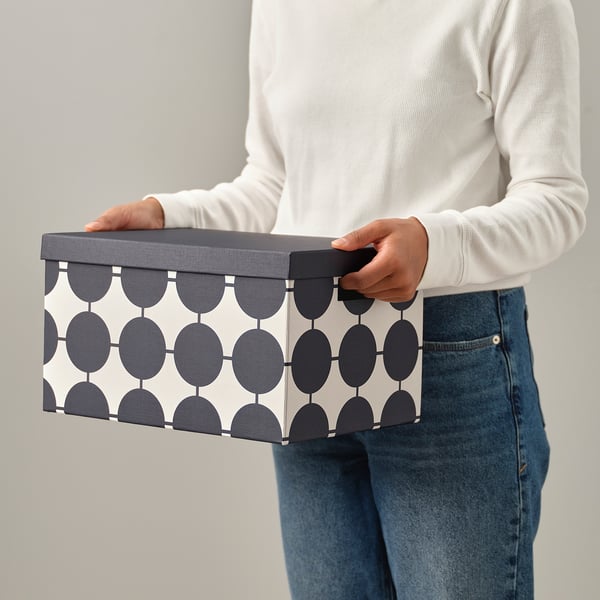 Persoon met een TJENA opbergdoos met een geometrisch patroon. De doos heeft een handvat voor gemakkelijke toegang.