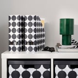 Stippen TJENA tijdschriftenhouder in zwart en wit op bureau met lamp & boeken.