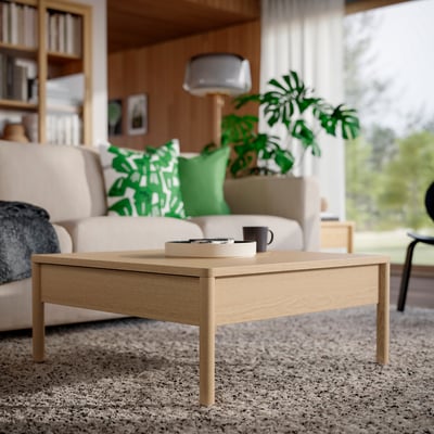 Bruin eiken fineer salontafel met zijladen op beige tapijt in gezellige woonkamer met bank, plant en boekenplank.