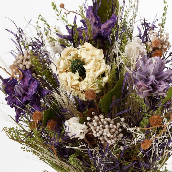 Gedroogd bloemenboeket met crème, paarse en bruine stelen met delicate bloemen en cilindrische zaaddozen, op natuurlijke wijze gerangschikt.
