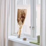 Gedroogde bloemen in bruin papier op vensterplank met zandloper en boek.