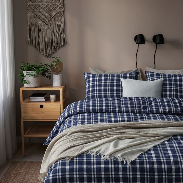 Blauw flanellen dekbed op bed met deken, nachtkastje met planten, boeken, lamp, wand decor.