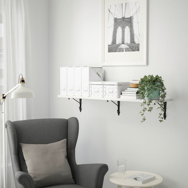 Gezellig hoekje met TRANHULT plank, boeken, plant en fauteuil. Brooklyn brug afdrukken boven, minimalistisch decor.