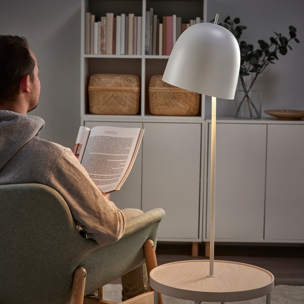 De mens leest in groene stoel door moderne lamp. Witte lamp op houten tafel naast hem, met opbergruimte erachter.