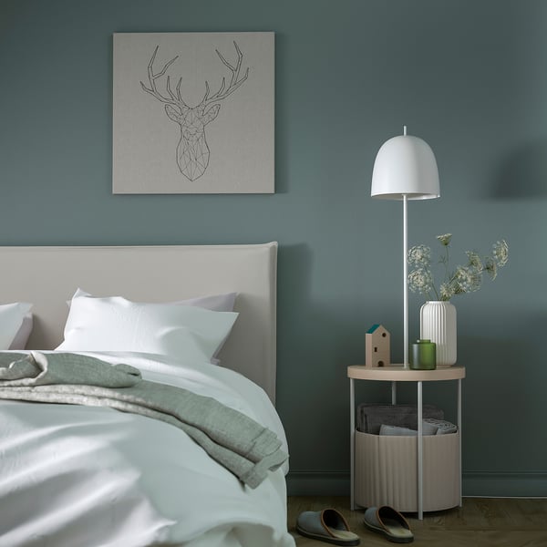 Minimalistische slaapkamer met TRINDSNÖ unit. Witte lamp, bijzettafel, opbergmand. Blauwgroene muren, pastelkleurige accenten.