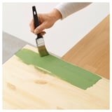 De persoon schildert houten oppervlakte met groene verf gebruikend een TRIXIG-borstel, die het vlot toepast.