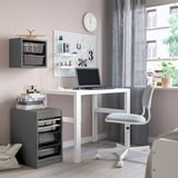 Kleine, grijze TROFAST opbergbakken georganiseerd onder een wit bureau, als aanvulling op ander meubilair in een gezellige kamer.