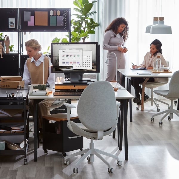 Drie vrouwen werken aan compacte TROTTEN-bureaus in een licht kantoor.