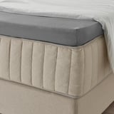 Bed met grijs hoeslaken, beige linnen rok met textuur, elastische rand, ziet er zacht en ademend uit.