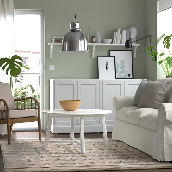 Moderne woonkamer met groene muren, houten vloer, vloerkleed, witte meubels en planken.