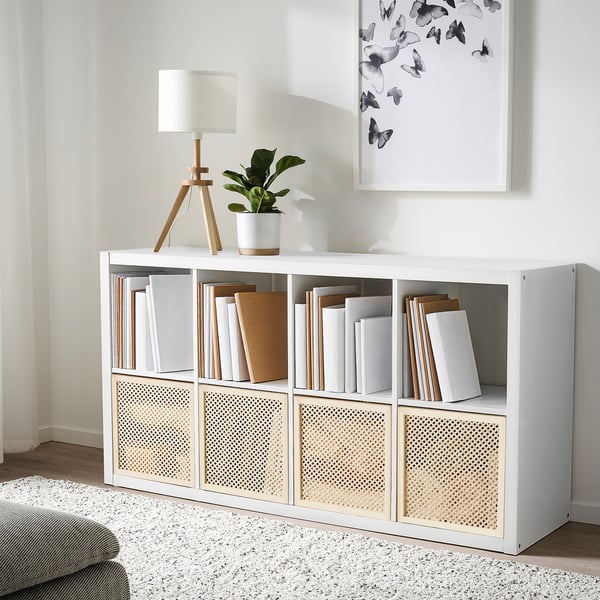 Een witte kubusorganizer met boeken en decoratie. Het bevat een lamp, een plant en een vlinderposter.