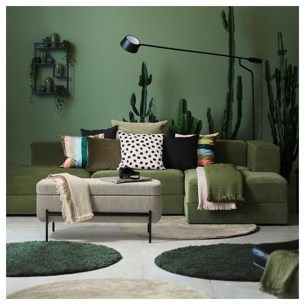 Moderne woonkamer met groene VALTORP bank, kleurrijke kussens, cactus decoraties en een gezellig vloerkleed.