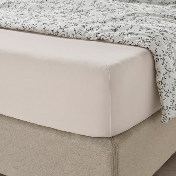 VÅRVIAL hoeslaken in lichtbeige op netjes opgemaakt bed, bedekt met gebloemd dekbed voor een gezellige nachtrust.