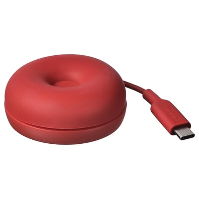 Rode, donutvormige draadloze oplader van ikea, gemaakt van zachte siliconen, met een usb-c kabel.