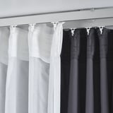 Afbeelding toont VIDGA-gordijnbeugels die witte en zwarte gordijnen ophangen, wat dubbellaagse licht- en privacycontrole demonstreert.