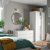 Moderne slaapkamer met groenblauw beddengoed, witte meubels, ronde spiegel en groene plant.