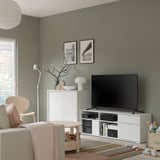 Moderne woonkamer met wit tv-meubel, beige stoel, kleurrijk vloerkleed en groene muren.