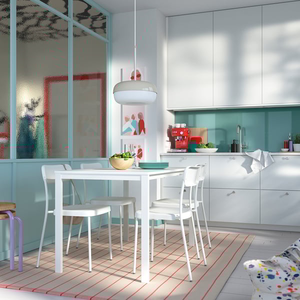 Lichte keuken met witte VIHALS tafel en stoelen. Grote ramen, blauwe accenten, houten schalen en kleurrijk tapijt.