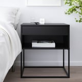 Zwart VIKHAMMER nachtkastje met lade, plank en soft-close lade, naast bed, met boeken en wekker.