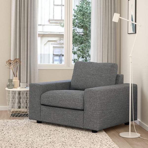 Grijze VIMLE accentstoel, lamp, bijzettafel met vazen, door groot raam met gordijnen. Gezellige, minimalistische kamer met vloerkleed.