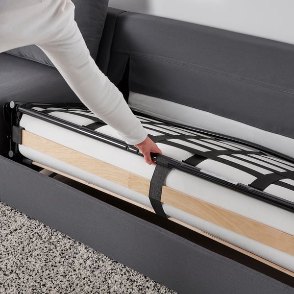 Een persoon past een slaapbankmechanisme aan, verlengt een dikke matras en demonstreert de gemakkelijke transformatie van bank naar bed.
