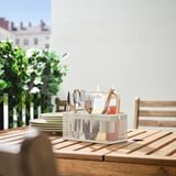 VIMPELFISK bestek organizer op houten tafel met RVS keukengerei, kleine flesjes, borden en plantenachtergrond. Compact en stijlvol.