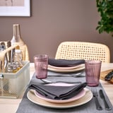 Eettafel met VIMPELFISK bamboe & stalen bestekhouder, borden, roze glazen en grijze servetten. Roze stoelen op de achtergrond.