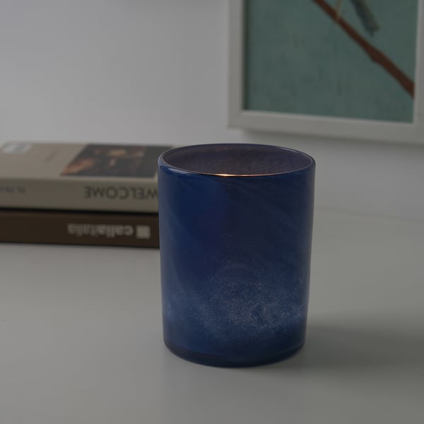 Blauwe glazen kandelaar op een tafel met een boek en een fotolijst.