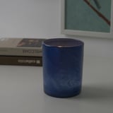 Blauwe glazen kandelaar op een tafel met een boek en een fotolijst.