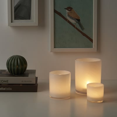 Drie VINDSTILLA kaarsen in matglas op tafel met boeken, kleinste vooraan, doorschijnend glas.