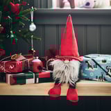 Een feestelijke VINTERFINT rode kerstman pluche zit op planken, kleiner dan ingepakte cadeaus en omgeven door feestelijke decoraties.