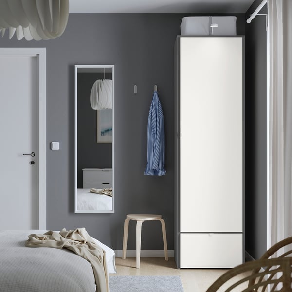 Moderne minimalistische slaapkamer met hoge witte VISTHUS kledingkast, blauwe handdoek, klein krukje, grote spiegel, wit bed, grijze muren.