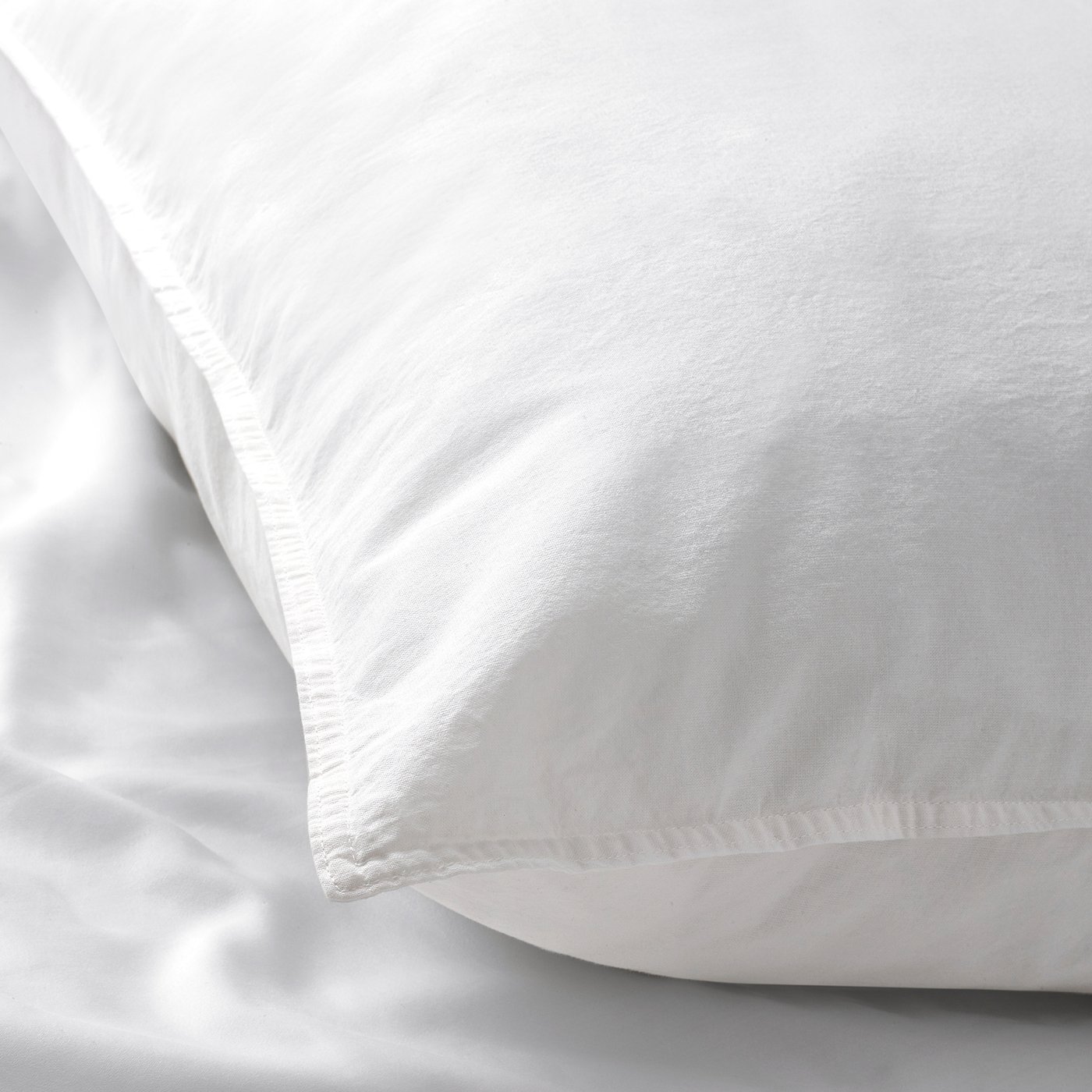 Close-up of soft, white cotton pillowcase. Envelope closure, smooth texture visible, suggesting high-quality material.