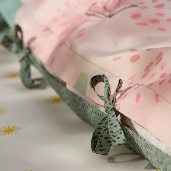Close-up of pink duvet cover with green nature print and bow.