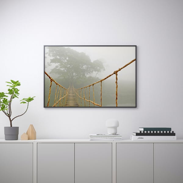 Framed art print of a bridge in fog, displayed on wall above cabinet with decorative items.