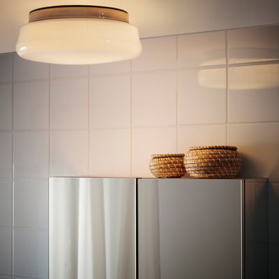 A modern bathroom with a round ceiling light providing diffused light, and two wicker baskets atop a cabinet.