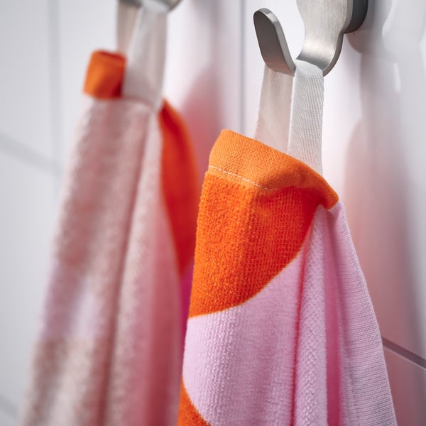 Colourful orange and pink striped towel hanging on a white hook, displaying soft fabric and quick drying capability.