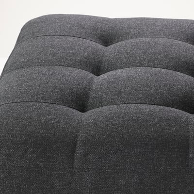Dark grey upholstered footstool with plush, wavy cushions and tight fabric fit.