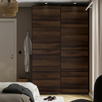 Modern bedroom with large brown wooden sliding wardrobe, white bedding, hanging coat, and wicker basket.