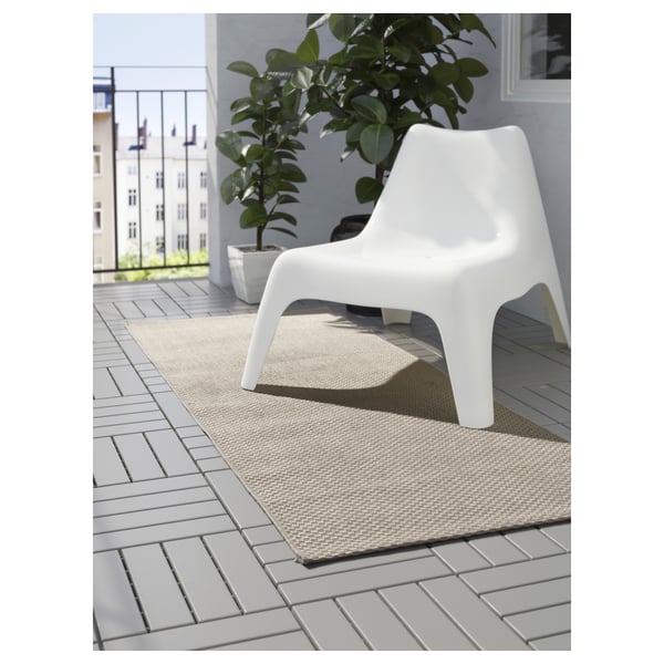 A modern, minimalist white chair on a beige outdoor rug on a grey tiled balcony, offering a cosy spot to relax.
