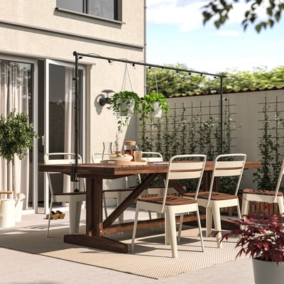 Outdoor dining setup with acacia table, metal chairs, plants, and lights. Perfect for patios.